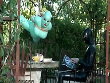 Girl In Green Latex Hangs Over Table Outdoors