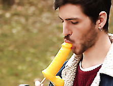 Handsome Man Is Sitting On The Bench Where He Is Sucking On A Lollipop That Is Shaped Like A Dick